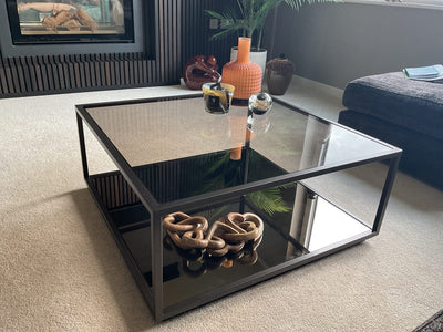 smoked glass square coffee table with metal edge and legs in a contemporary home setting.